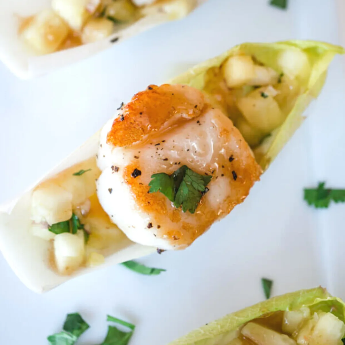 Top down view of a seared scallop appetizer recipe sitting on top of pineapple salsa inside an endive leaf. - hostess at heart