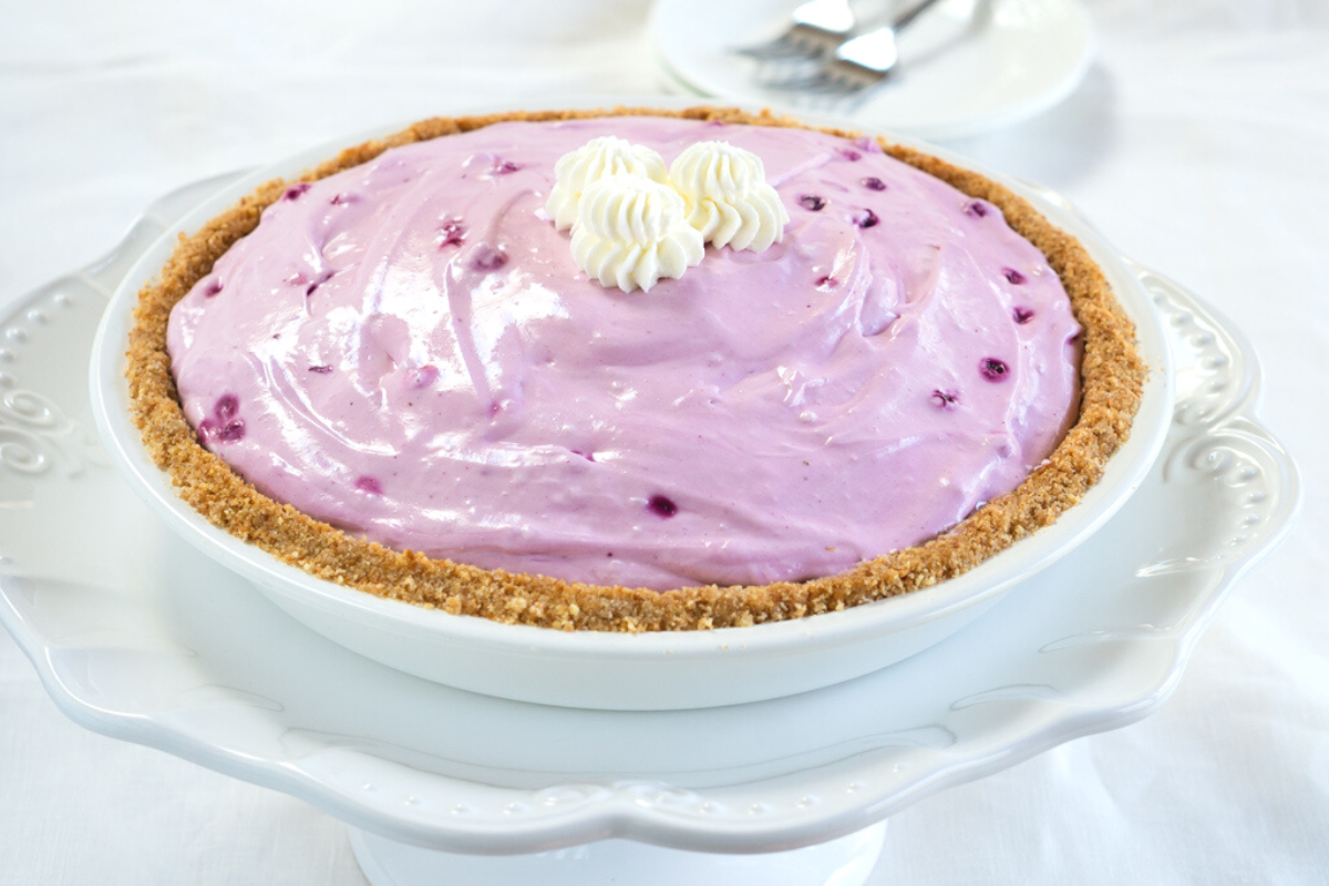 Angled view of a purple hued creamy pie filled with blueberries in a crumb crust.