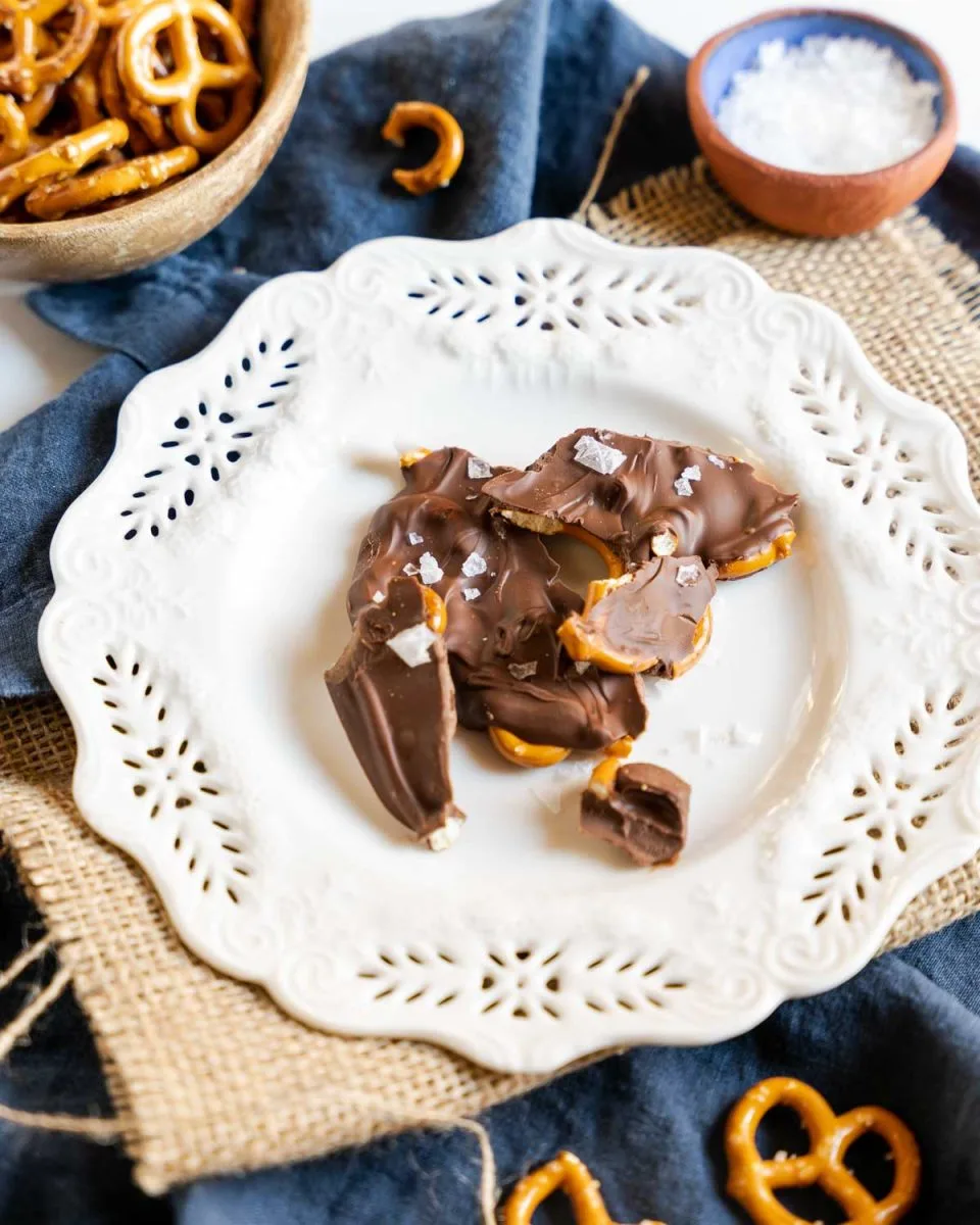 a white plate containing pieces of chocolate covered pretzels sprinkled with sea salt - hostess at heart