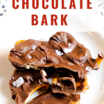 Pieces of Chocolate Bark Covered Pretzels sprinkled with sea salt sitting on a white plate. Hostess At Heart