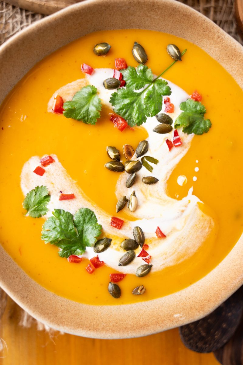 Close-up view of a bowl of Pumpkin Thai Soup topped with cilantro, pepitas, and red pepper.