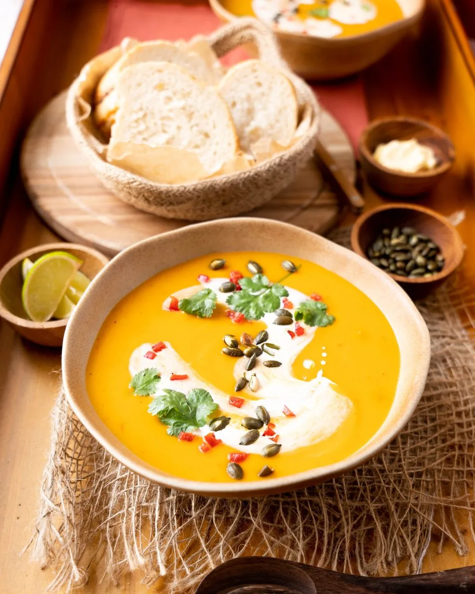 An angled view of Pumpkin Thai Soup with a coconut swirl topped with pepitas and cilantro.