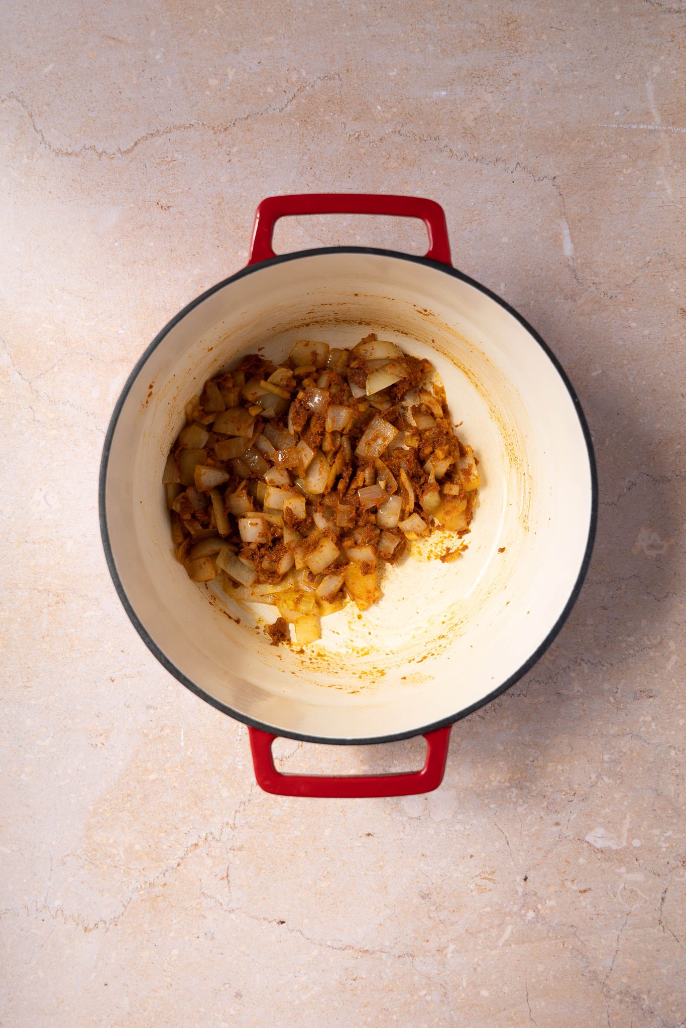 Top down view of red curry added to sauteed onion in a dutch oven