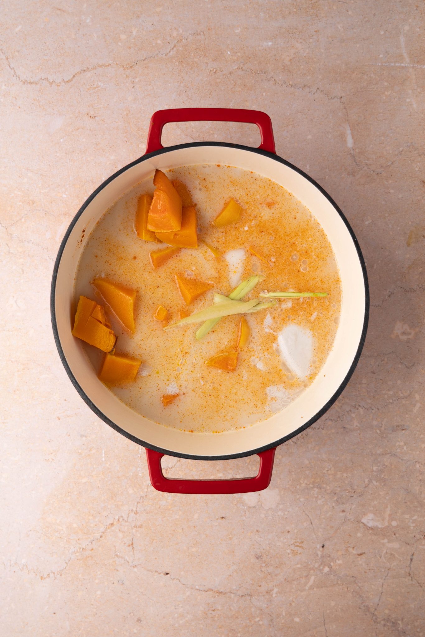 Top down view of roasted pumpkin, sauteed onion, coconut milk and lemon grass in a dutch oven.