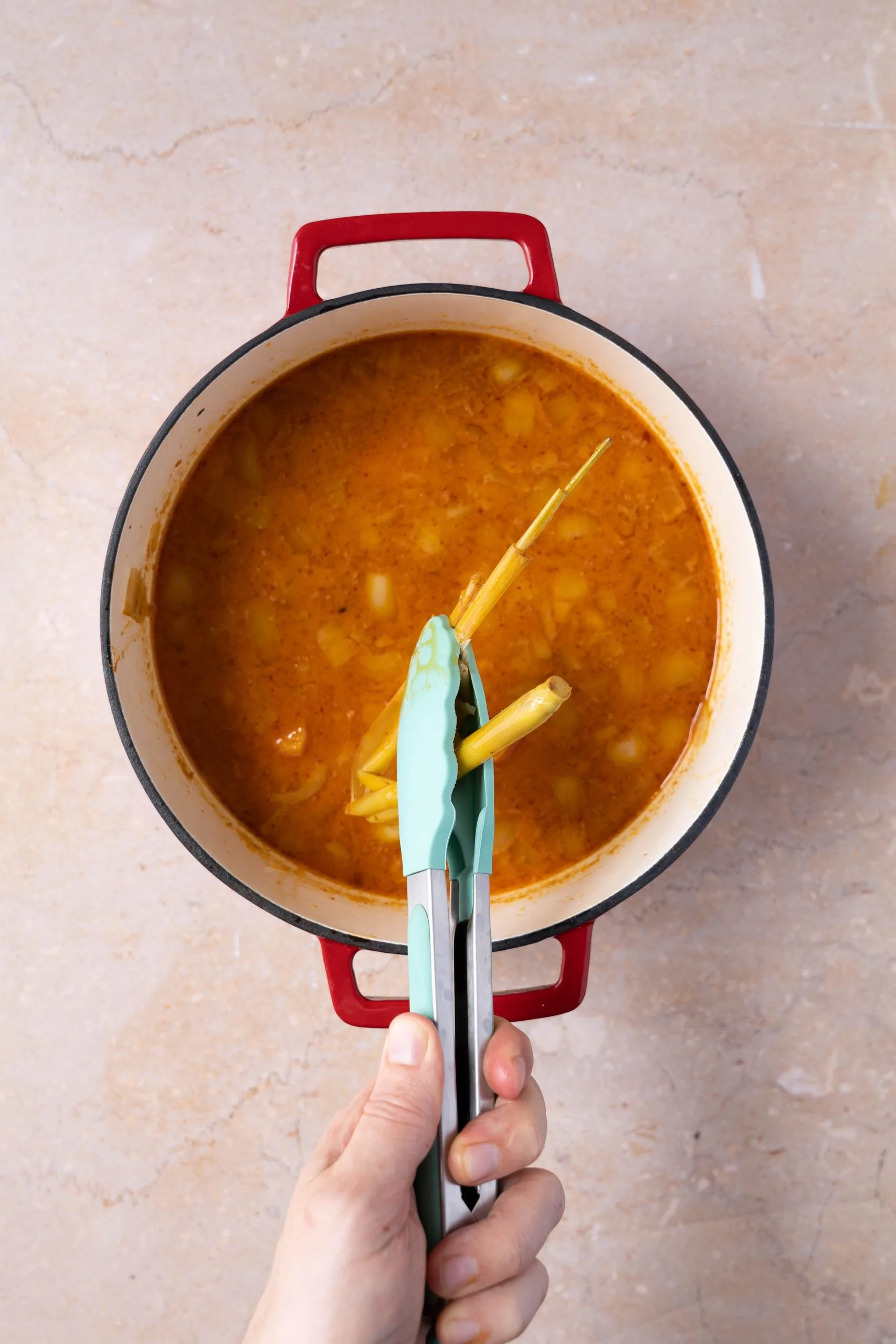 A stalk of lemon grass removed from soup with tongs.