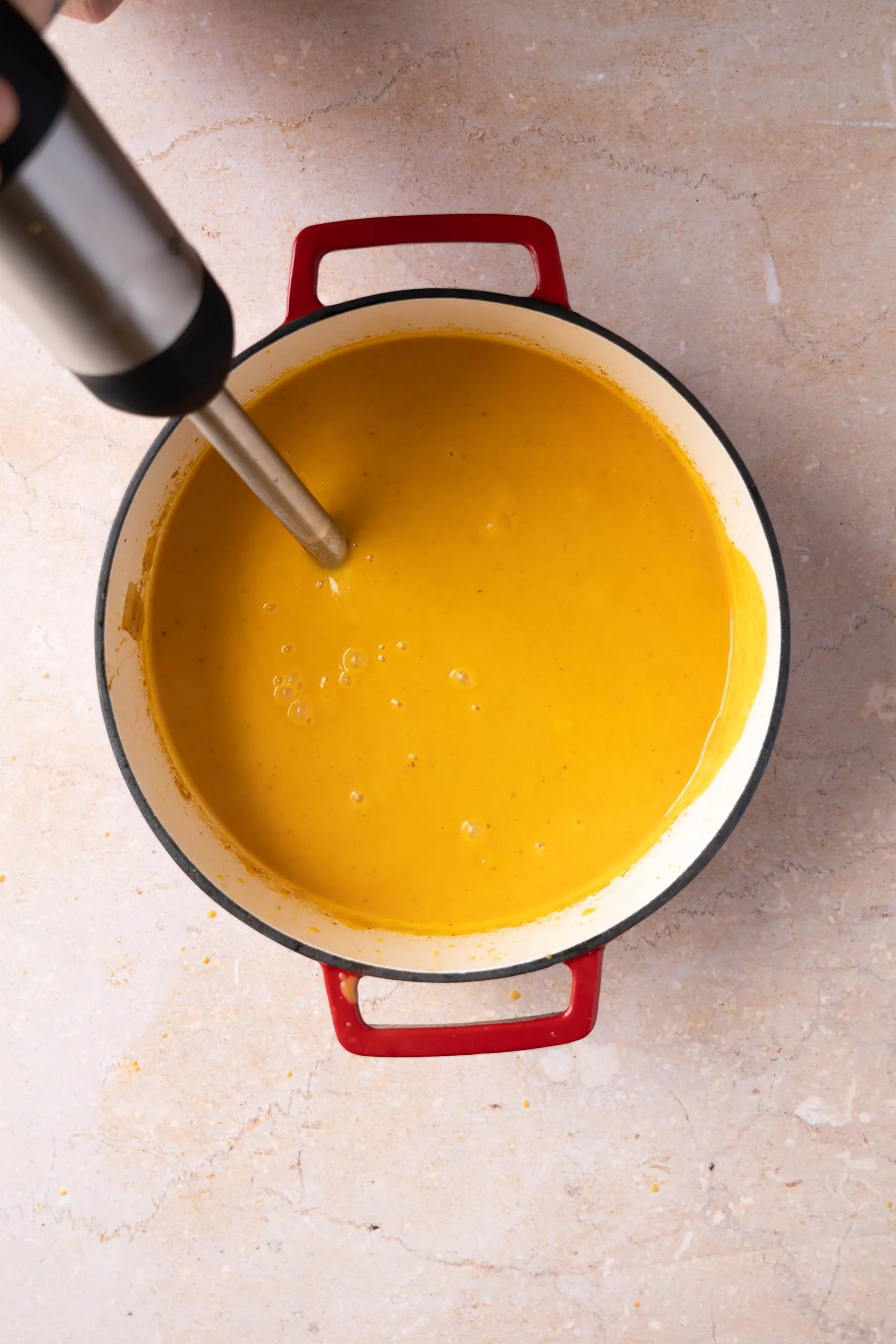 An immersion blender blending pumpkin soup ingredients in a dutch oven.
