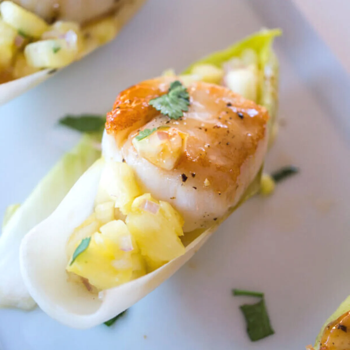 Angled view of scallop appetizer recipe witting on pineapple salsa in an endive leave. Hostess At Heart