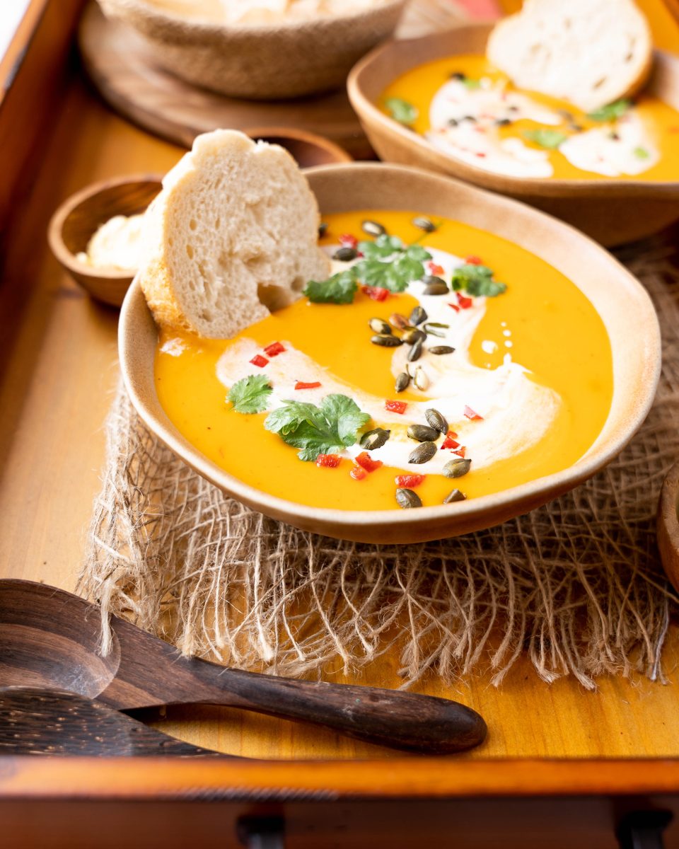 Angled view of thai red curry pumpkin soup topped with peppitas and a swirl of coconut milk.