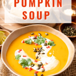 3/4 angled view of a bowl of pumpkin soup topped with pepitas, cilantro and diced red pepper.
