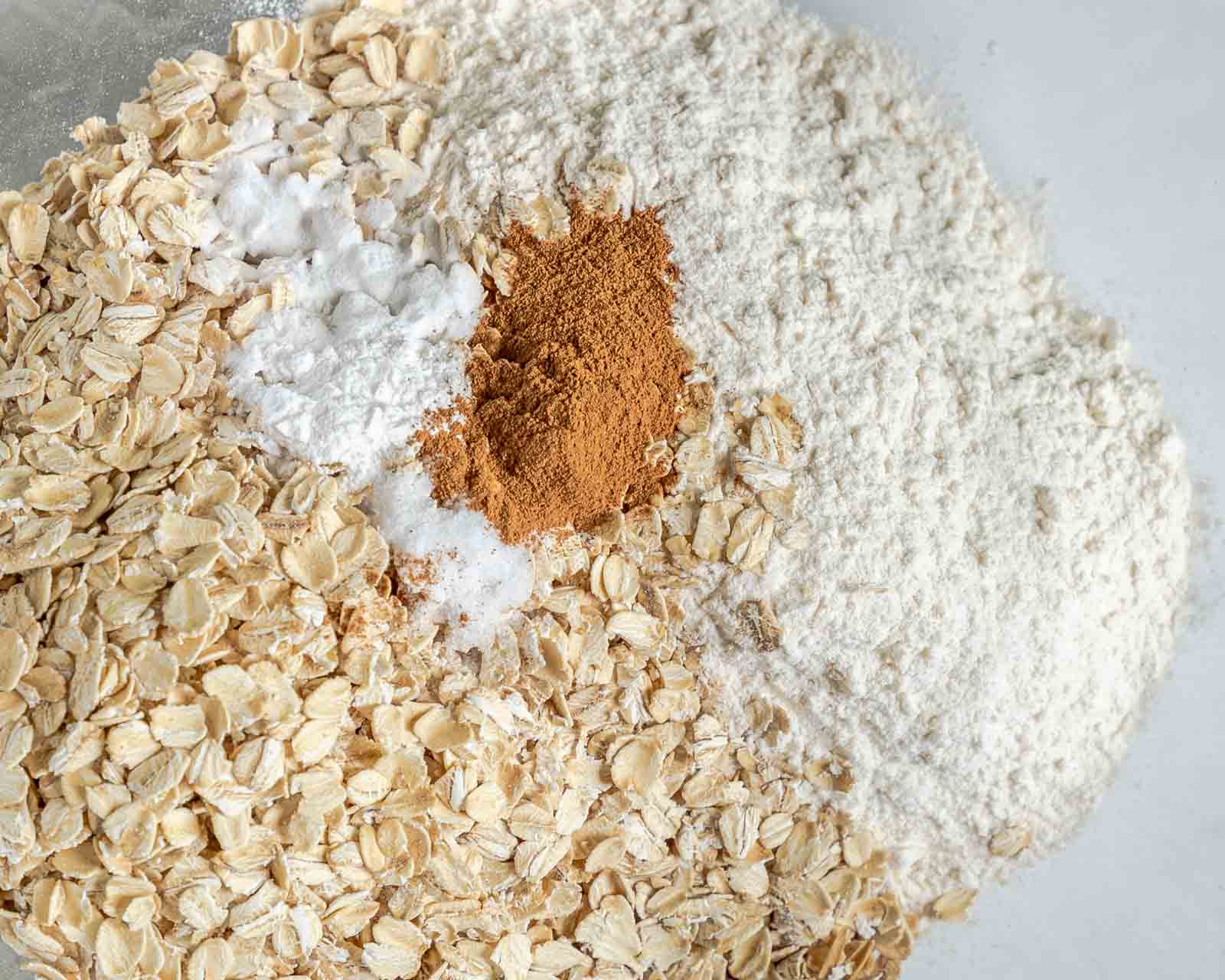 Dry ingredients added to a bowl including oats, flour, cinnamon, baking soda, salt and baking powder.