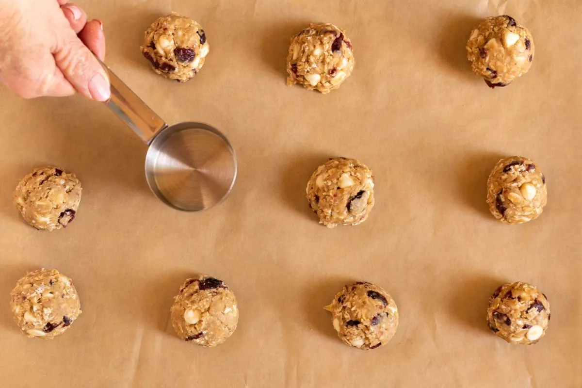 Cookie dough balls on a baking sheet flattened with a measuring cup.