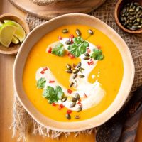 Top down view of a bowl of roasted pumpkin curry soup topped with cilantro, coconut milk swirl, red pepper, and pepitas.