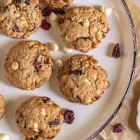 Top down view of white chocolate cranberry oatmeal cookies sitting on a white plate over parchment paper.