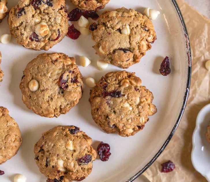 Top down view of white chocolate cranberry oatmeal cookies sitting on a white plate over parchment paper.
