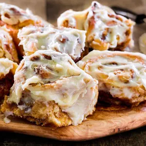 Close up view of a homemade cinnamon roll dripping with icing on a cutting board surrounded by more rolls baked from scratch - Hostess At Heart