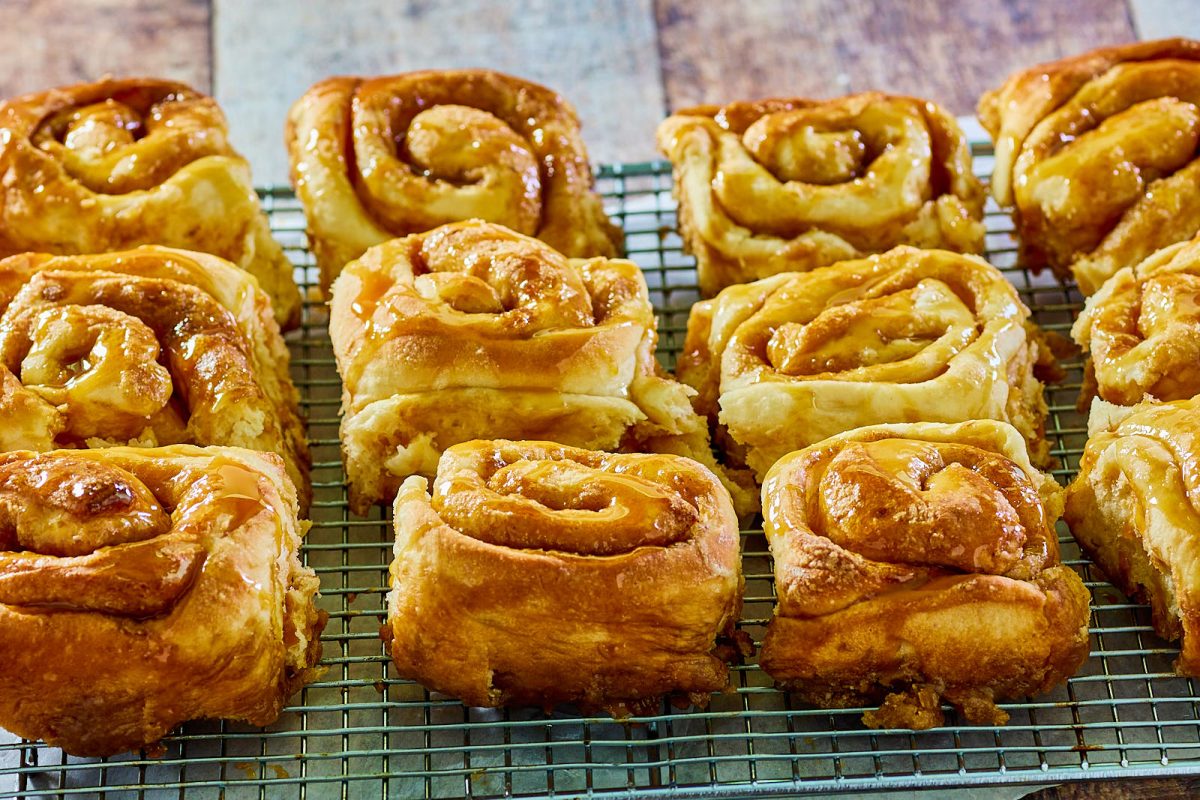 Side view of soft and tender baked caramel rolls sitting on a cooling rack - Hostess At Heart