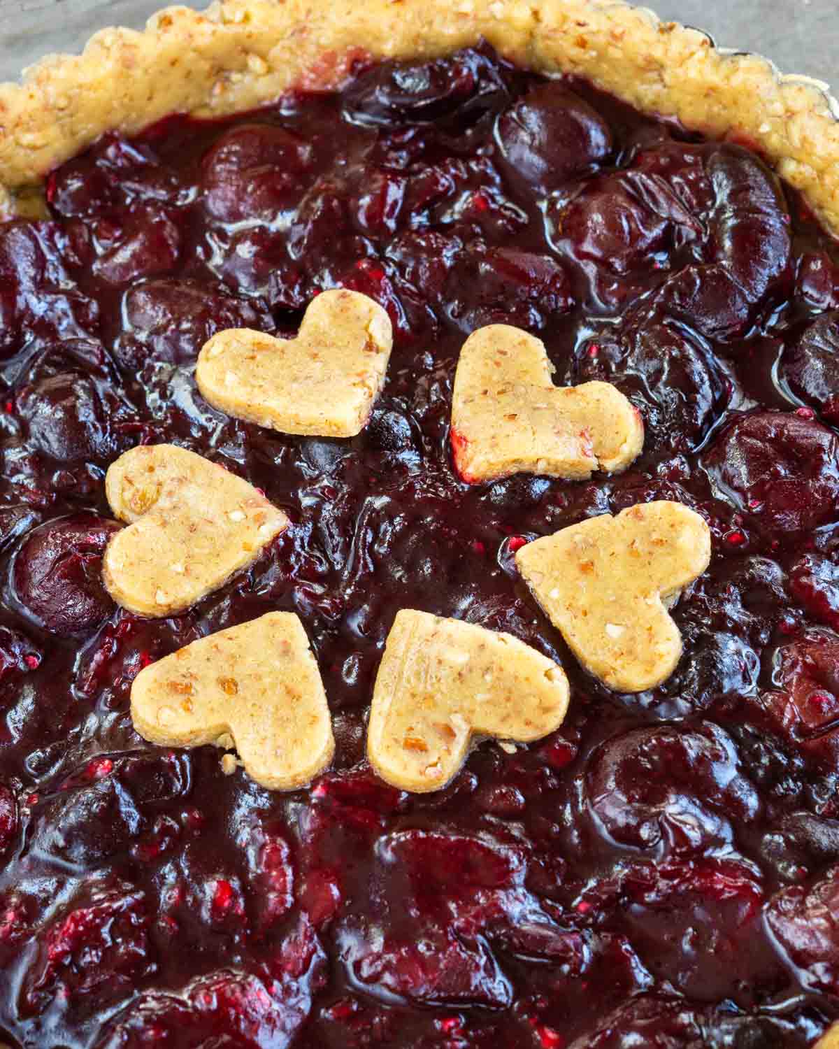 Close up of an unbaked cherry tart with pastry hearts decorating the center. Hostess At Heart