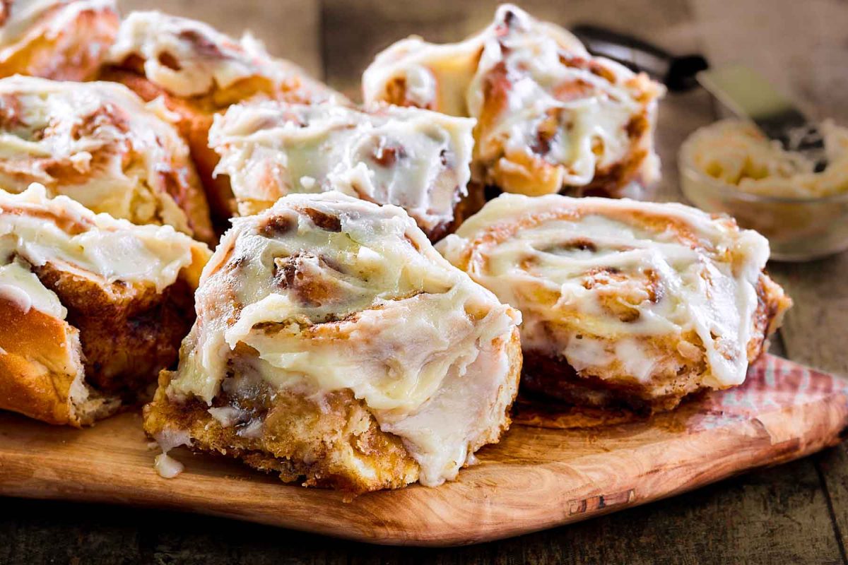 Front view of cinnamon rolls covered in frosting sitting on a cutting board