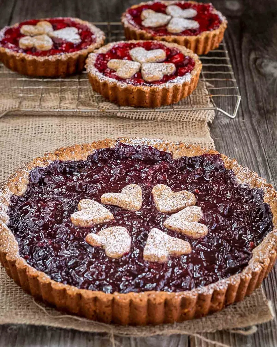 A large Sweet Cherry Torte sits in front of individual cherry tarts. Hostess At Heart