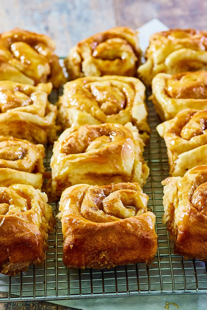 Angled view of baked rolls covered with caramel on a cooling rack - Hostess At Heart