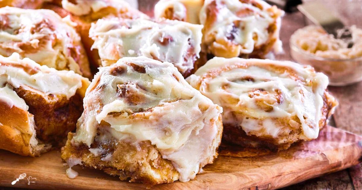 Front view of homemade cinamon rolls covered in icing sitting on a cutting board - hostess at heart