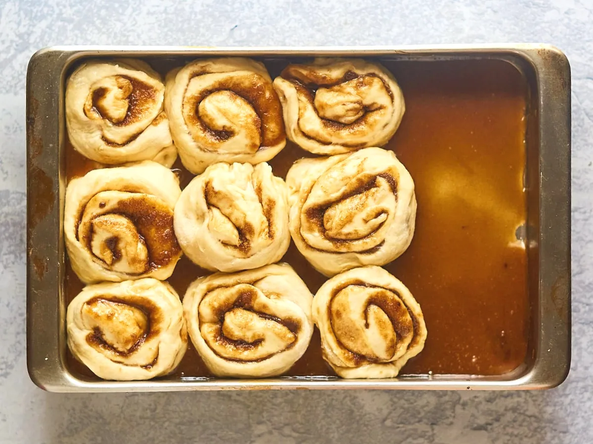Unbaked rolls filled with cinnamon sitting on a pan over a layer or caramel. Hostess At Heart