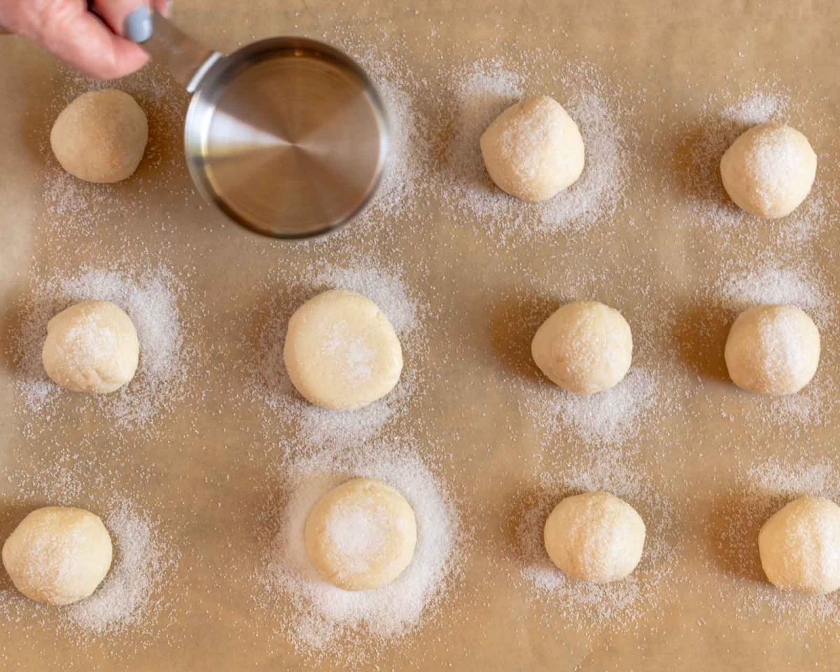 Top down view of balls of cookie dough sprinkled with sugar sitting on parchment paper. Hostess At Heart