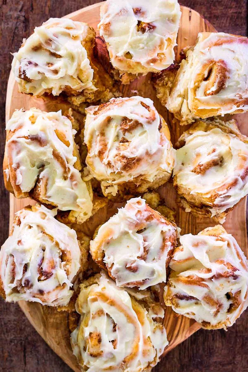 Top down view of cinnamon rolls topped with frosting covering a cutting board - Hostess At Heart