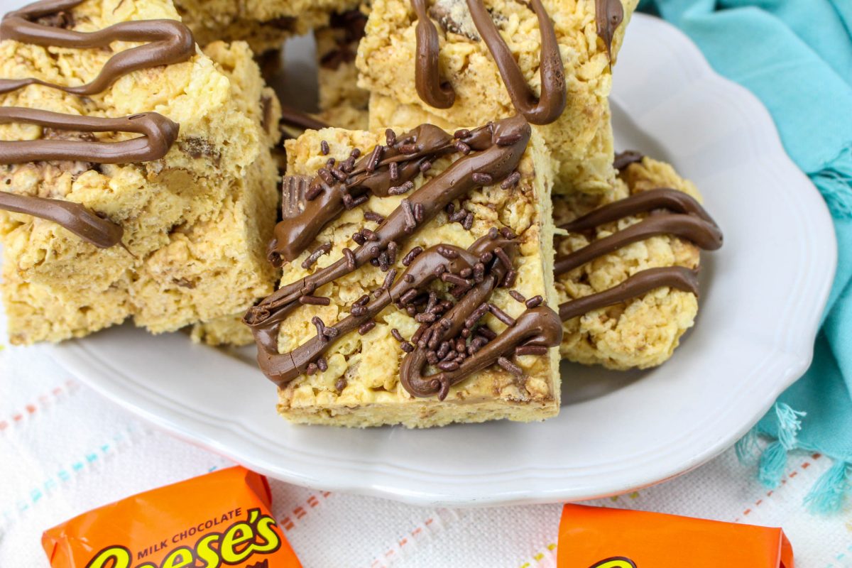 Table view of peanut butter rice crispy treats drizzled with dark chocolate on a plate.