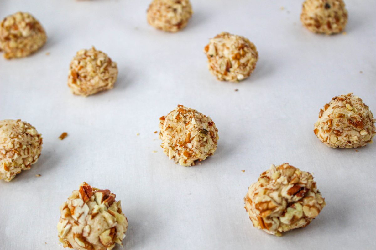 Turtle Thumbprint Cookie dough shaped into balls and rolled into nuts on a cookie sheet. Hostess At Heart