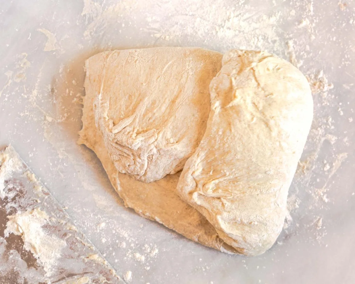 The right side of bread dough stretched and folded to the center in order to shape it.