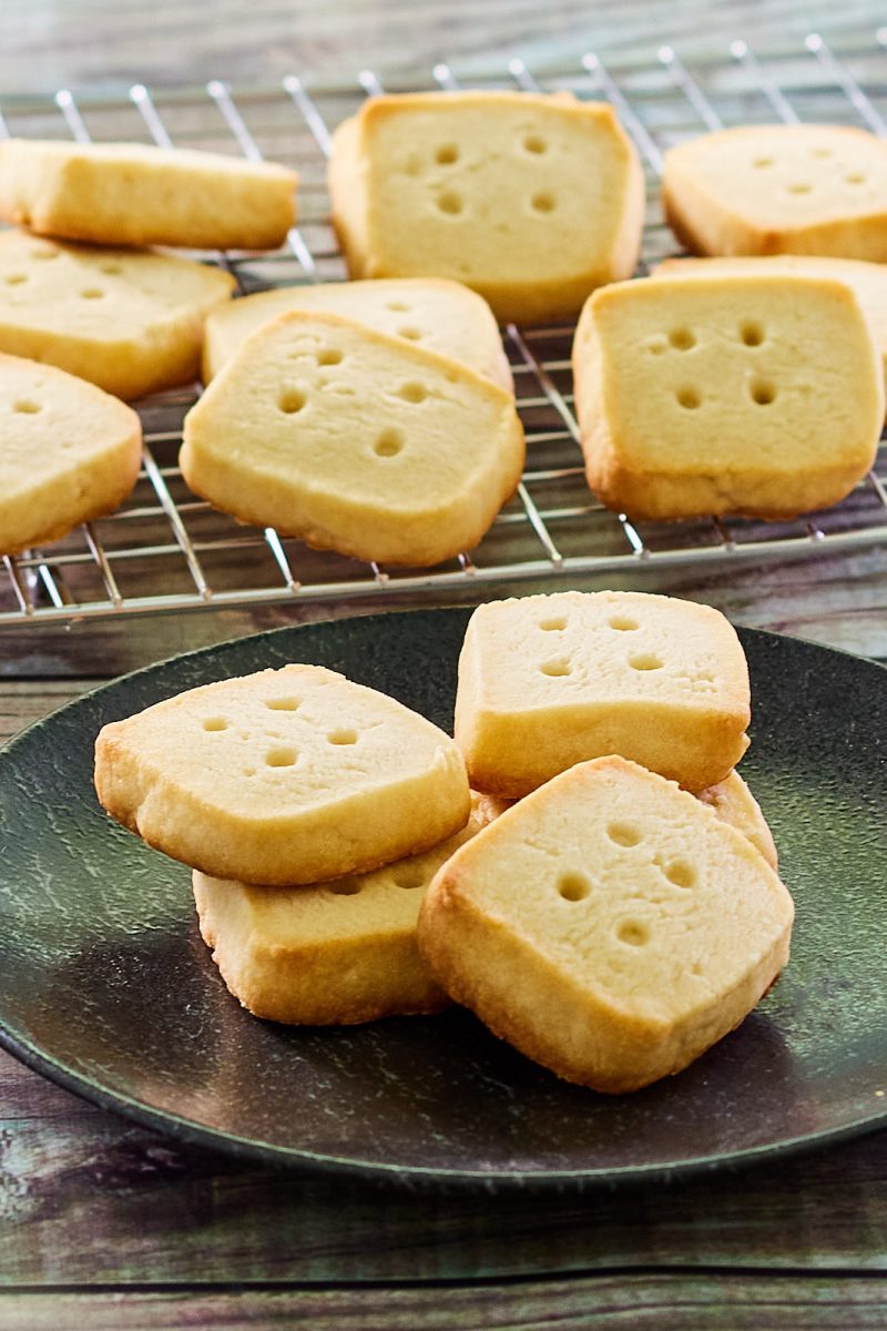 Short bread cookies on a plate in front of a rack of baked cookies - hostess at heart