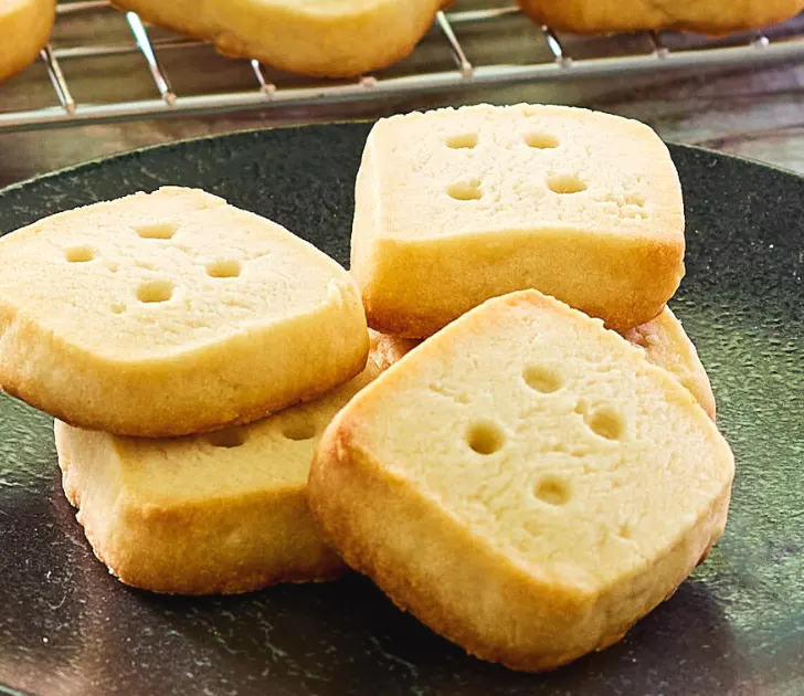 A stack of shirtbread cookies that look like dice on a dark-colored plate - hostess at heart