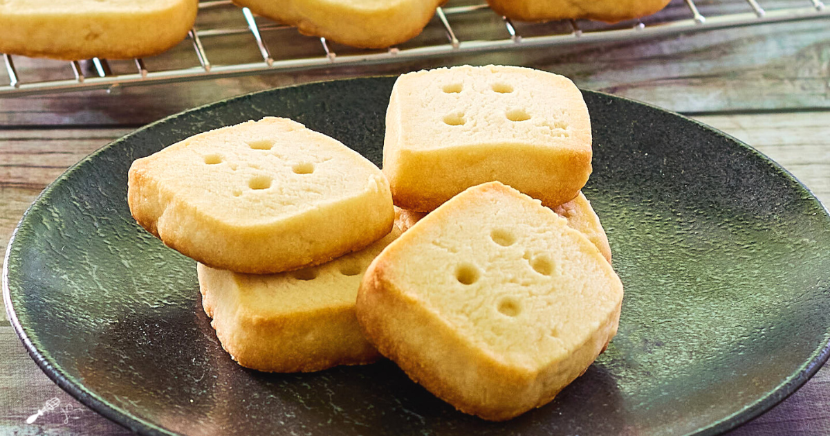 A stack of shirtbread cookies that look like dice on a dark-colored plate - hostess at heart