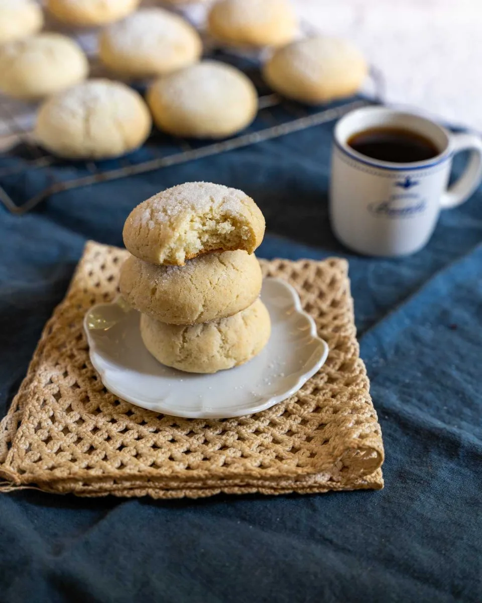 Sour cream sugar cookies stacked on a white plate with a bite taken out of the top one. Hostess At Heart