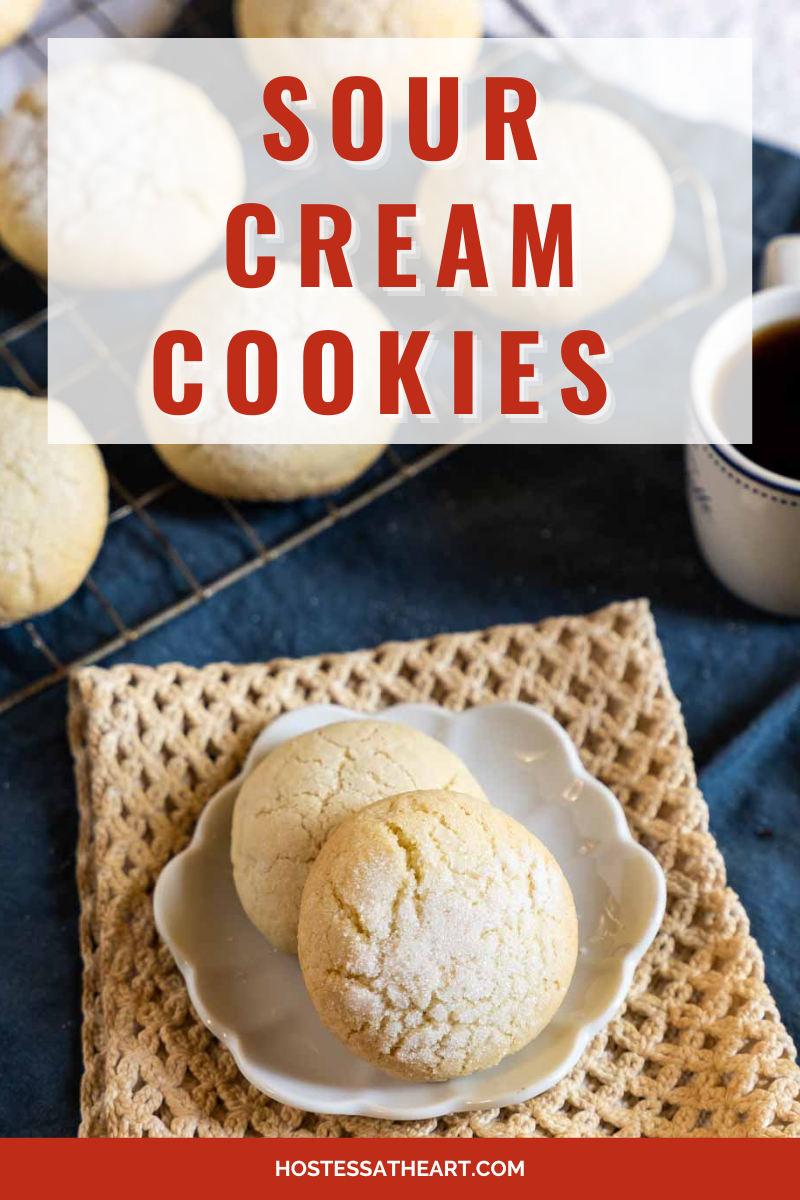 Sour Cream Cookie recipe baked into small cookies and coated in sugar sitting on a white plate with more cookies in the background on a cooling rack. Hostess At Heart