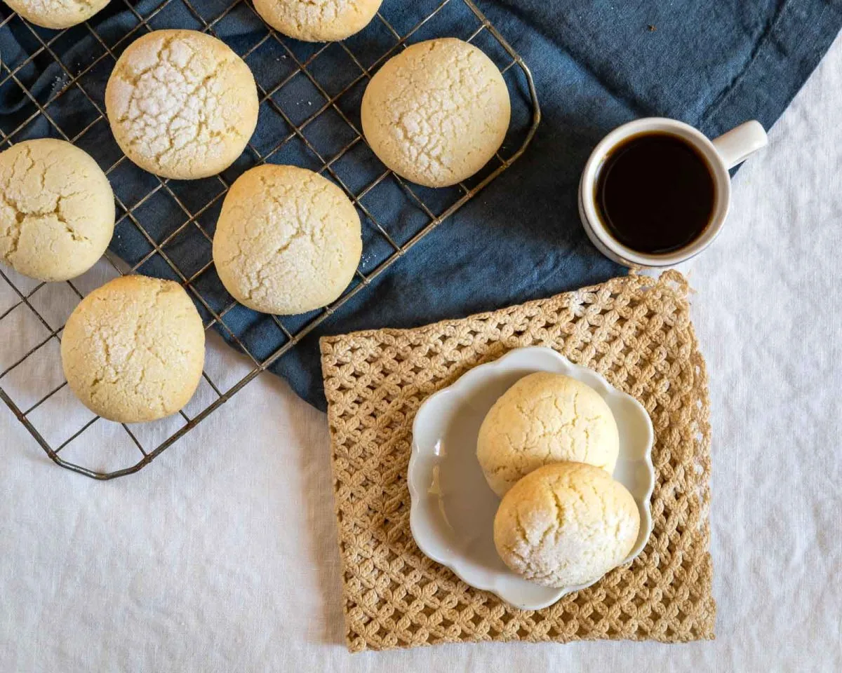 Top down view of Sugar cookies with sour cream sitting on a small white plate next to a cooking rack topped with bake cookies - Hostess At Heart