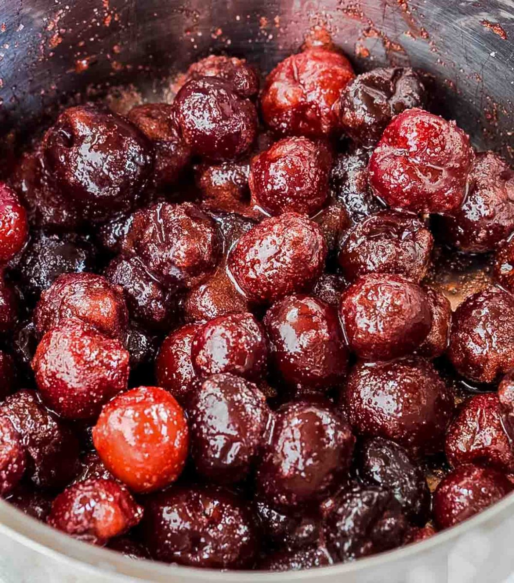 Top down view of cherries mixed with sugar cooking in a saucepan - hostess at heart