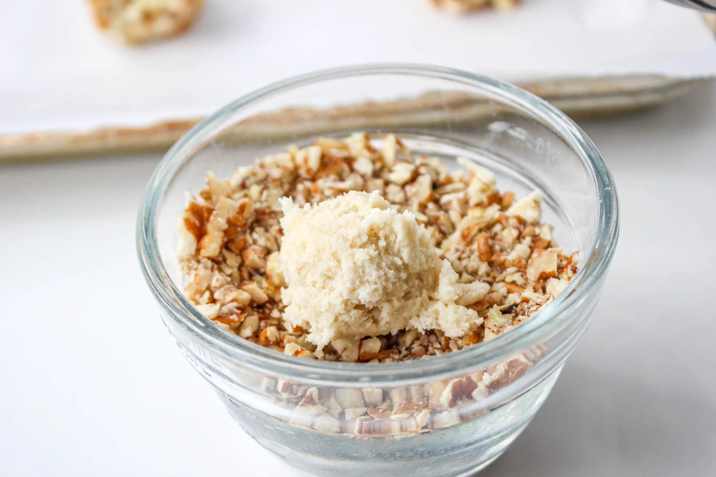 A bowl of crushed nuts with a Turtle Blossom Cookie dough ball ready to be rolled. Hostess At Heart