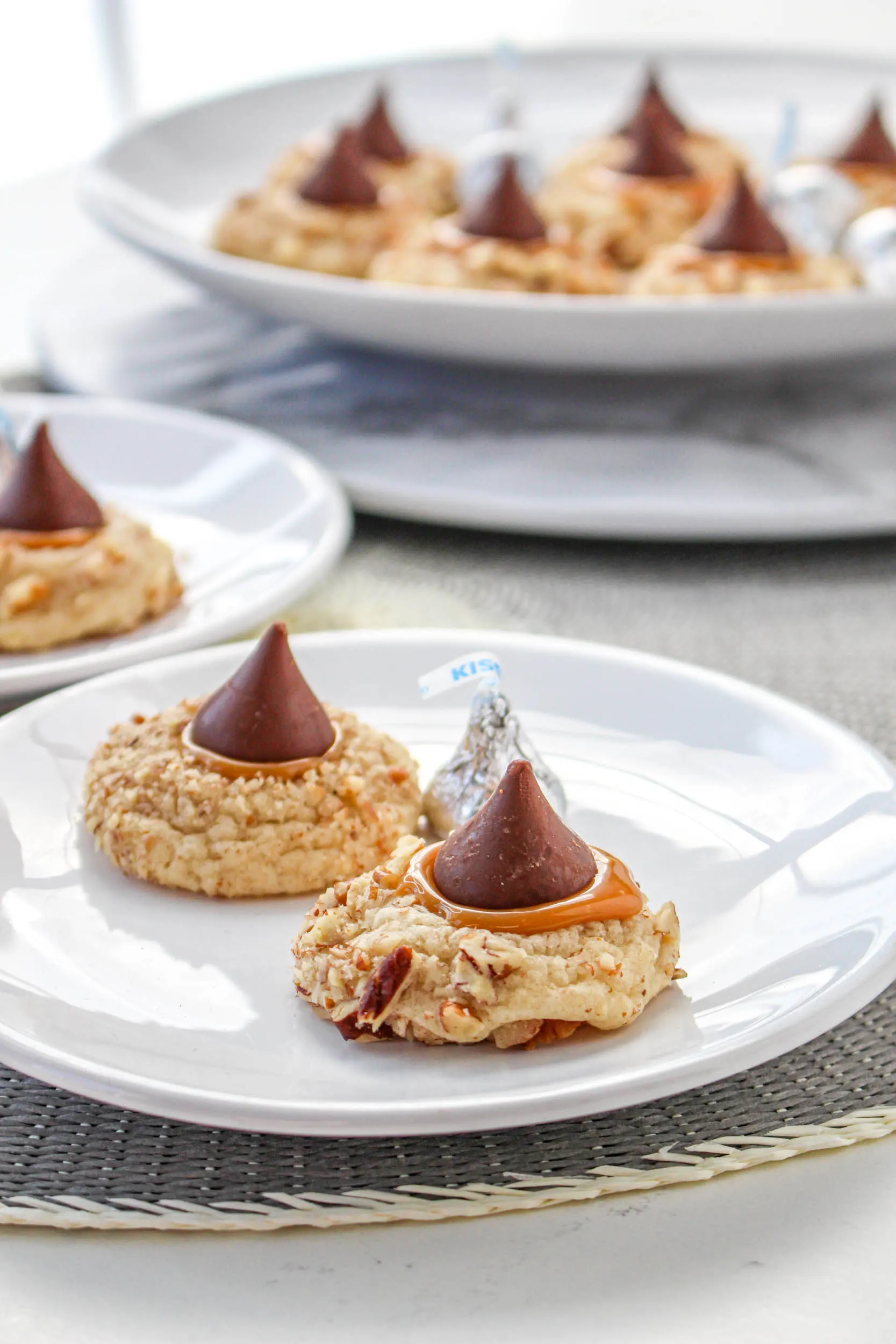 Tableview of two nut-rolled caramel-filled turtle thumbprint cookies sitting on a plate. Hostess At Heart