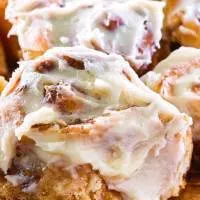 Close up view of Iced Cinnamon Rolls sitting on a cutting board.