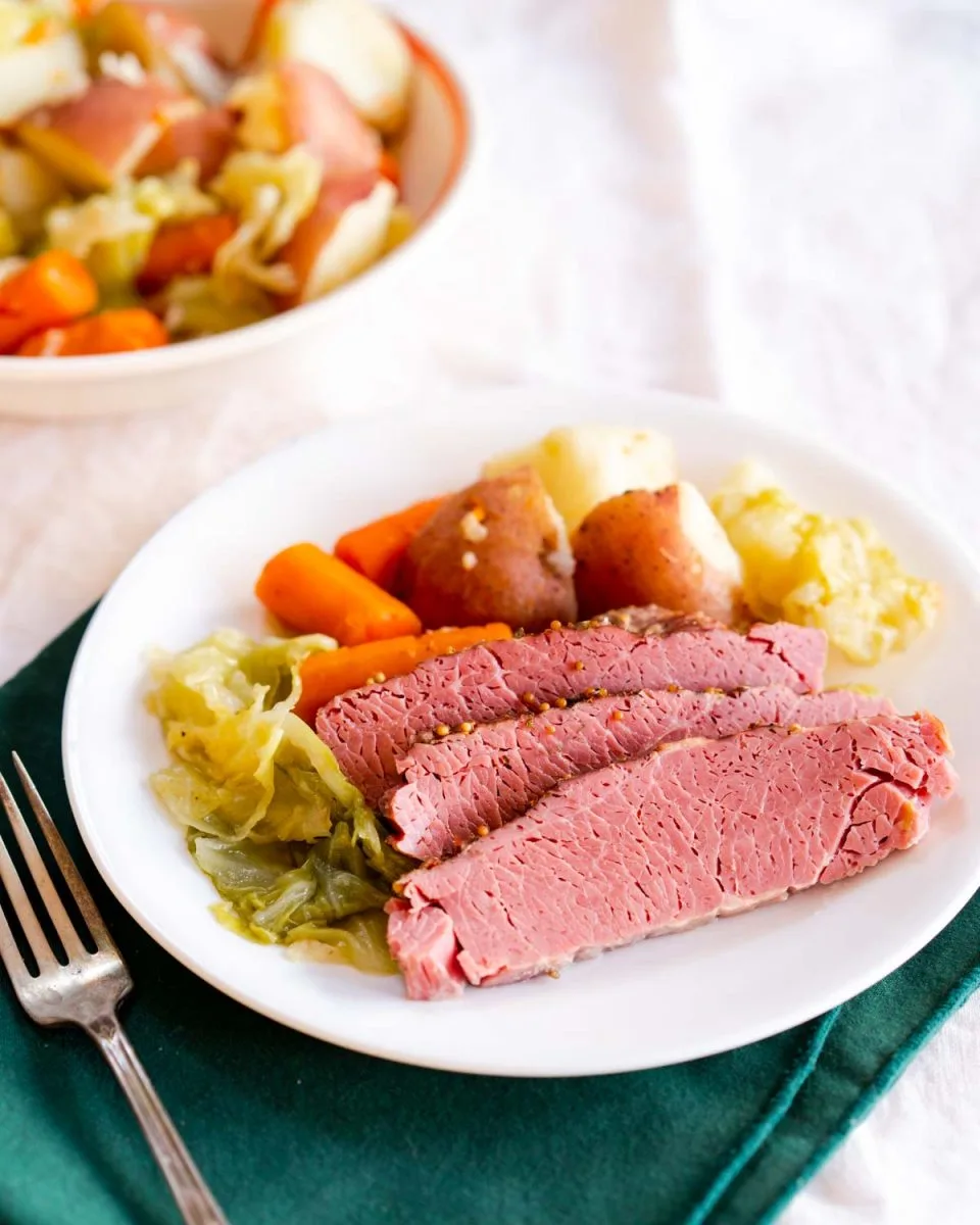 Juicy Corn Beef sliced on a plate and surrounded by veggies cooked in an insta pot - Hostess At Heart