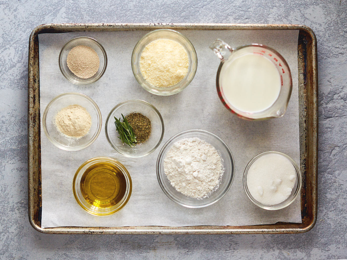 Ingredients used to make rosemary focaccia bread include sugar, yeast, milk, salt, flour, cheese, olive oil, and herbs. - Hostess At Heart