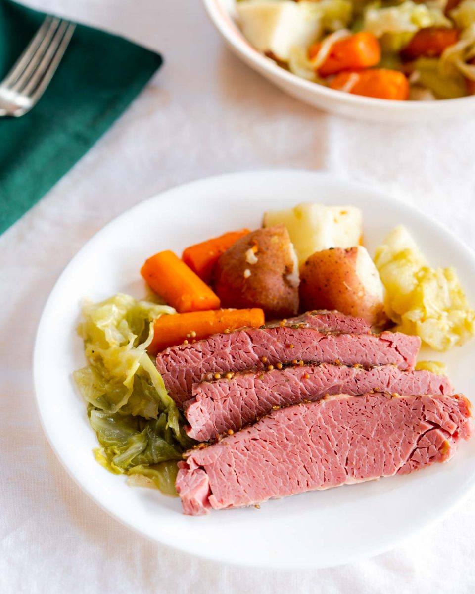 Top down view of sliced corned beef surrounded by cooked cabbage, carrots, and potatoes on a white plate - Hostess At Heart