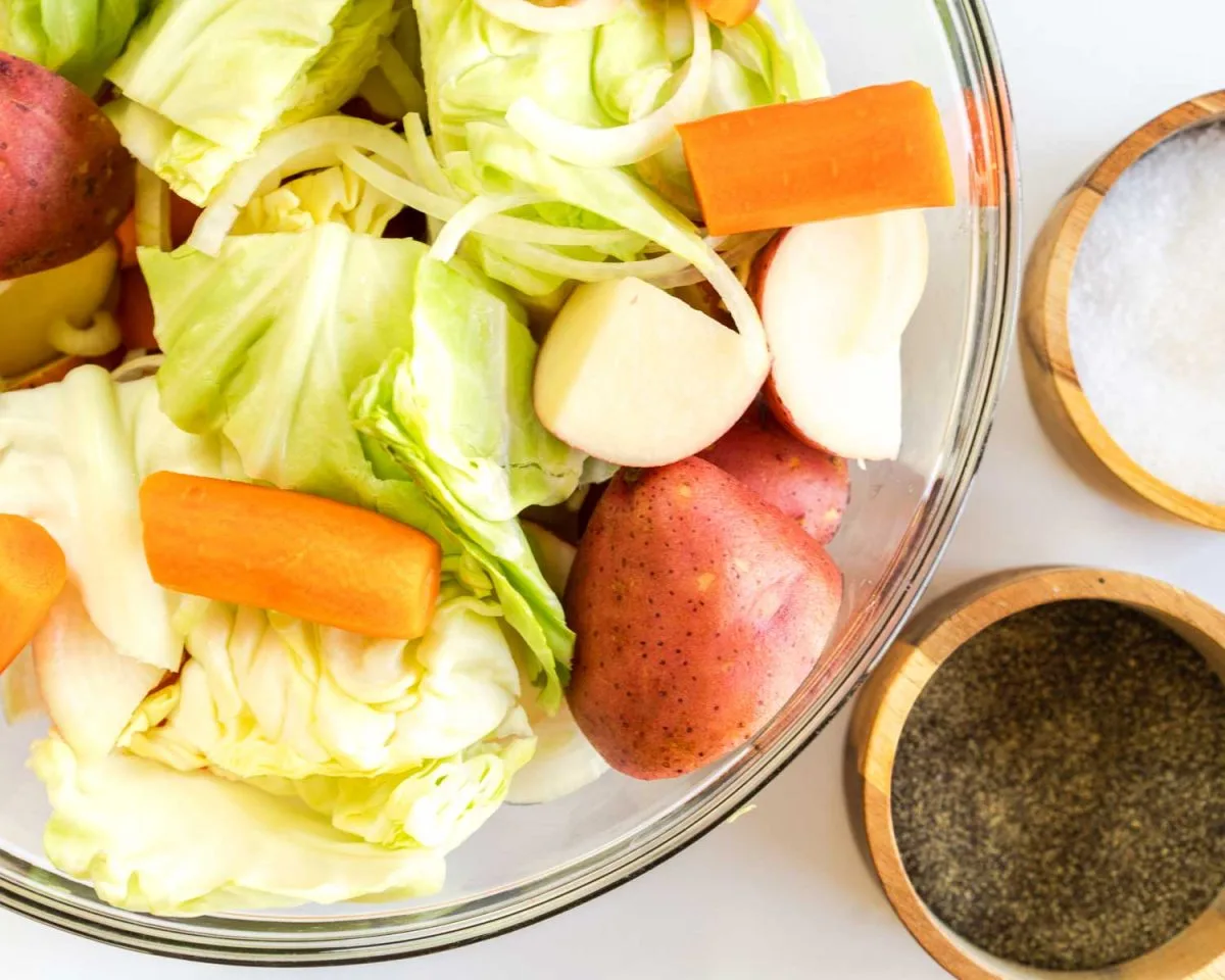 Cut carrots, potatoes, onion and cabbage in a bowl next to small salt and pepper dishes. - Hostess At Heart