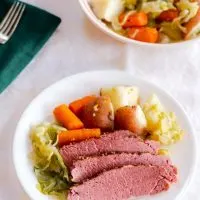 Sliced Instant Pot Corned beef sitting on a white plate surrounded by cooked cabbage, carrots, and Potatoes - Hostess At Heart