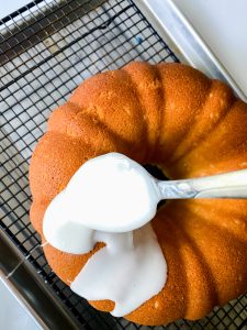 A large spoon applying glaze to a baked bundt cake - Hostess At Heart
