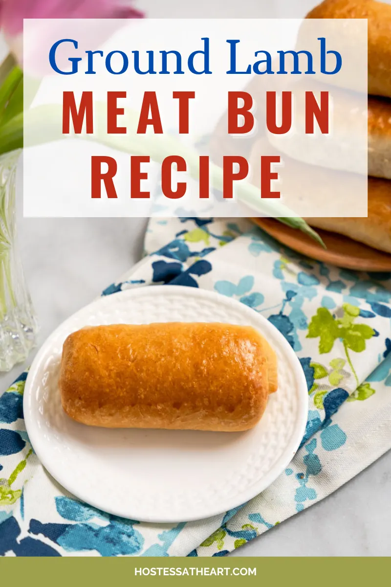 Top-down view of a baked bun filled with ground lamb and cheese. A plate of more meat buns sit in the background. The title appears for Pinterest - Hostess At Heart.