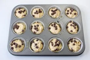 A muffin tin filled with Banana Peanut Butter Muffin batter. Chocolate chips are sprinkled over the top - Hostess At Heart