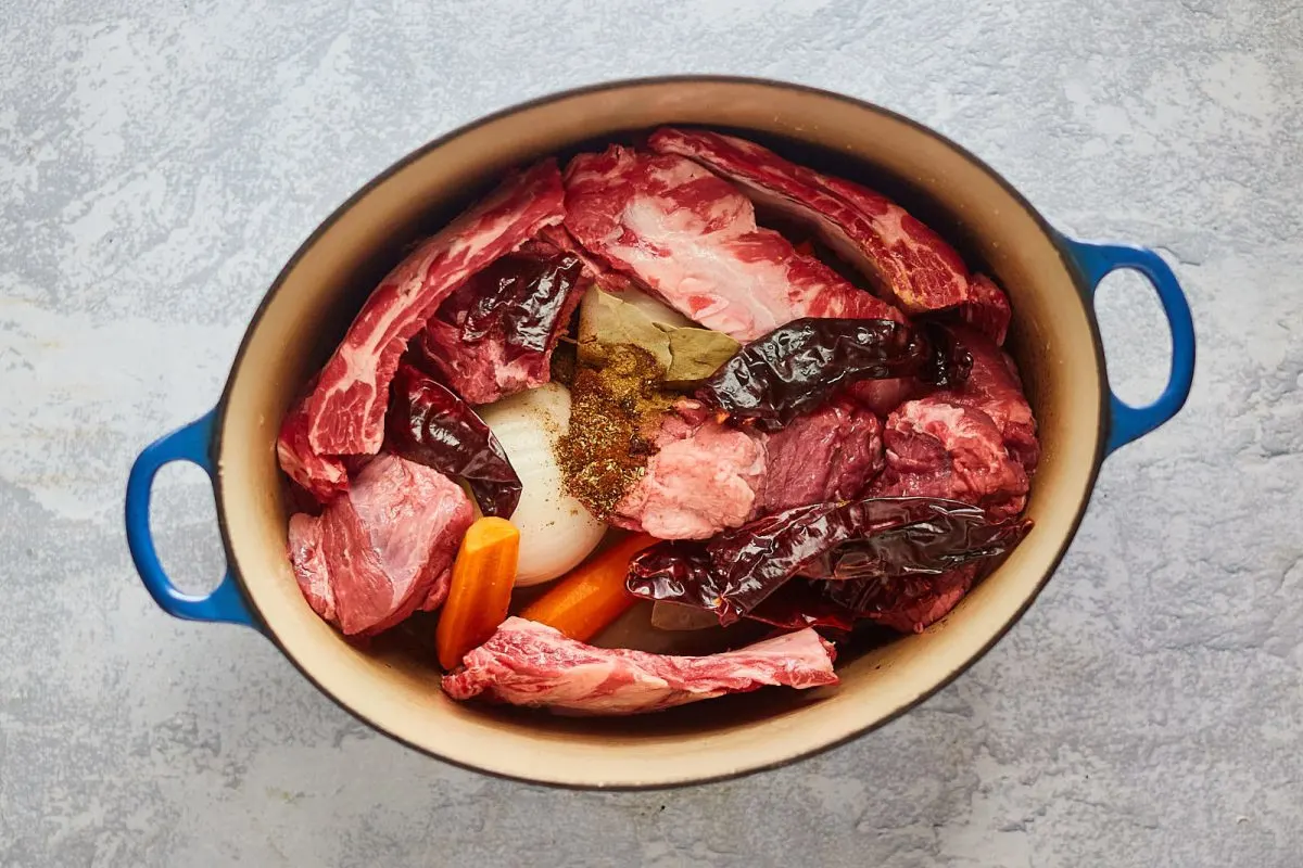 Dutch oven filled with meat, vegetables, dried peppers, and spices in preparation to make Birra tacos - Hostess At Heart